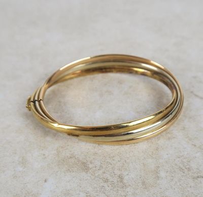 un gros plan d'un bracelet rigide en or posé sur une surface en marbre