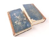two old books are sitting side by side on a white surface