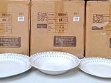 trois assiettes blanches et deux bols blancs sont posés sur une table, à côté d'une boîte de nourriture