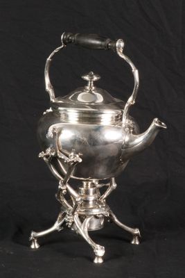 an antique silver tea kettle on a stand against a black background