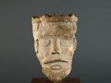 a close up of a sculpture of a man ' s face on a wooden stand