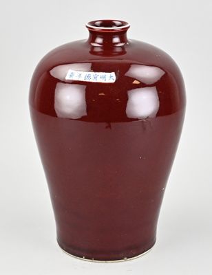 un vase rouge muni d'une étiquette, posé sur une table