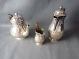 two silver teapots and a sugar shaker on a table