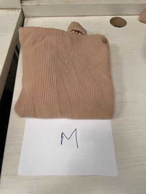 Le pull est de couleur beige et porte une étiquette sur laquelle est inscrit « m ».