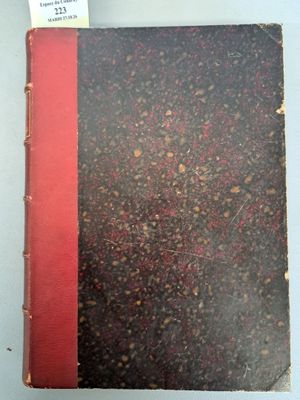 un vieux livre posé sur une table blanche à côté d'un livre rouge