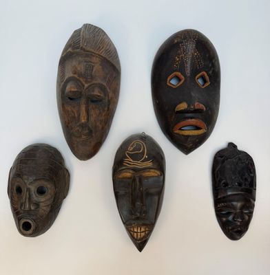 quatre masques en bois sont exposés sur une surface blanche