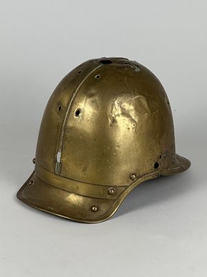 un vieux casque en laiton posé sur une surface blanche, avec un fond gris