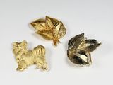 three gold and silver brooches with leaves and a dog
