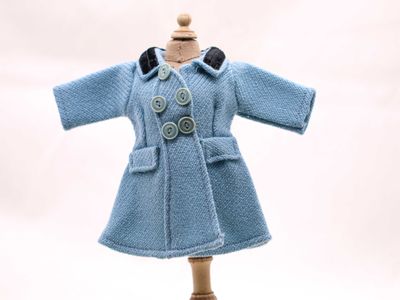 une poupée vêtue d'un manteau bleu, posée sur un socle en bois