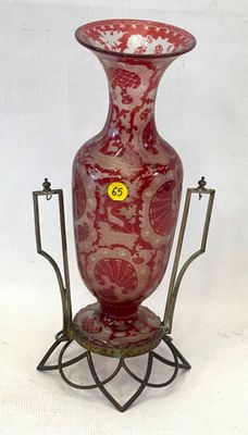 un vase rouge posé sur un socle, sur lequel est collé un autocollant jaune