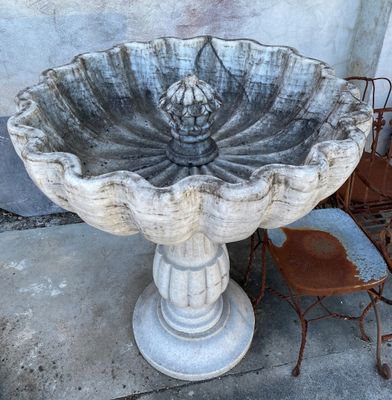 a bird bath sitting next to a chair on the sidewalk