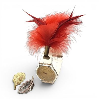 a watch with a red feather on it sitting next to a leaf