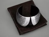 bracelet manchette argenté et noir posé sur un tissu marron, sur une surface grise