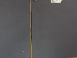 Le lampadaire est posé sur un parquet, devant un mur gris.