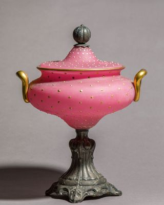 un vase rose et doré muni d'un couvercle, posé sur un socle
