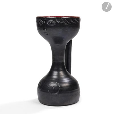 un vase noir surmonté d'un couvercle rouge, posé sur une surface blanche