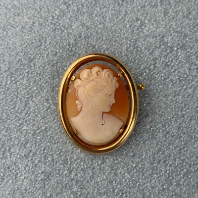 Une broche en or représente le profil d'une femme.