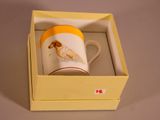 a yellow and white cup in a box with a picture of a dog on it