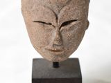 une sculpture en pierre représentant un visage, posée sur un socle en bois