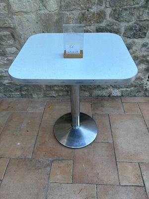 une table blanche avec un plateau en verre, posée sur un sol en briques