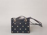 un sac à main noir orné d'étoiles dorées, posé sur une surface blanche