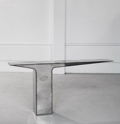 une table en verre transparent avec un piètement en métal, placée au milieu d'une pièce