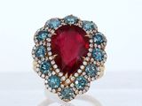 a close up of a ring with a red stone surrounded by blue and white diamonds