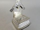 une petite horloge en argent posée sur un socle, sur une table