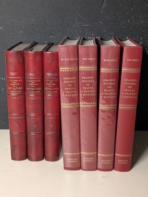 Plusieurs livres rouges sont alignés sur une étagère devant un mur noir.