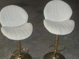 two white leather bar stools with gold bases in a garage