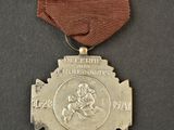 an old silver medal with a red ribbon on a black surface