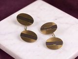 a close up of a pair of gold and blue striped cufflinks on a marble surface