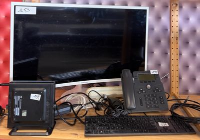 a desk with a monitor, keyboard, phone, and other electronics on it