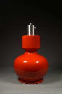 un vase orange surmonté d'un couvercle argenté, posé sur une surface grise