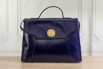 blue leather handbag with golden buckle on wooden table in front of white wall
