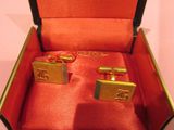 two gold cufflinks in a red box on a table