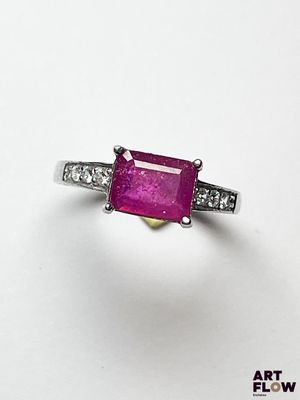 un gros plan d'une bague en pierre rose et diamants posée sur une surface blanche