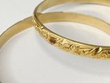 pair of gold tone bang bracelets with engraved designs on them