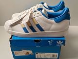 des chaussures Adidas Superstar blanches et bleues posées sur une boîte bleue