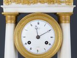 a white and gold clock on a pedestal with a black background