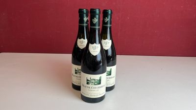 trois bouteilles de vin sont posées sur une table devant un mur rouge