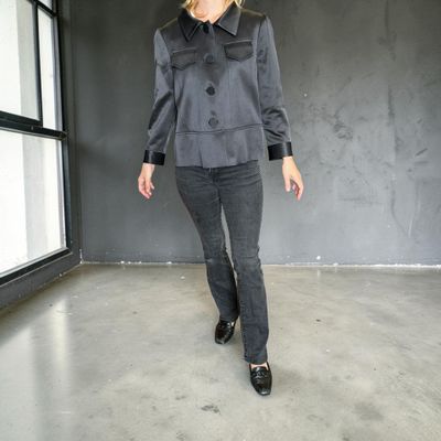 une femme debout dans une pièce, vêtue d'une veste grise et d'un pantalon noir