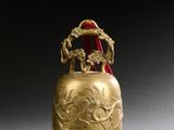 une clochette dorée richement décorée, à laquelle est accroché un ruban rouge au niveau du col
