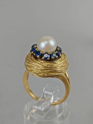 a close up of a gold ring with a pearl and blue sapphires