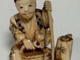 une petite figurine représentant un garçon avec un panier et un bâton