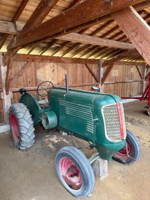 un tracteur vert garé dans une grange, avec un tracteur rouge derrière lui