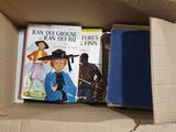 une boîte remplie de livres et une paire de chaussures par terre