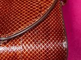 an image of a brown snake skin purse on a pink background