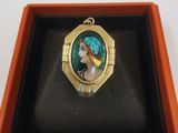 un gros plan sur une bague dans un écrin, avec la photo d'une femme