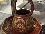 a red and gold cup and saucer sitting on a table